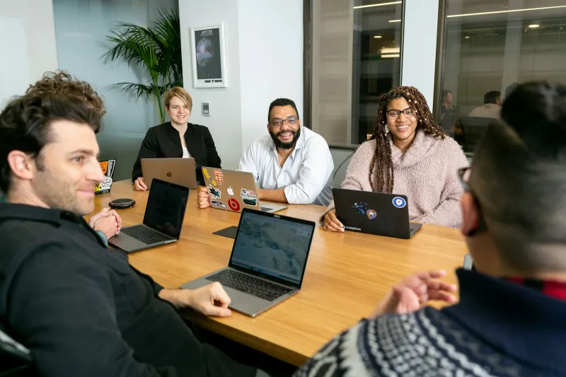 Diverse team collaborating around a meeting table with laptops